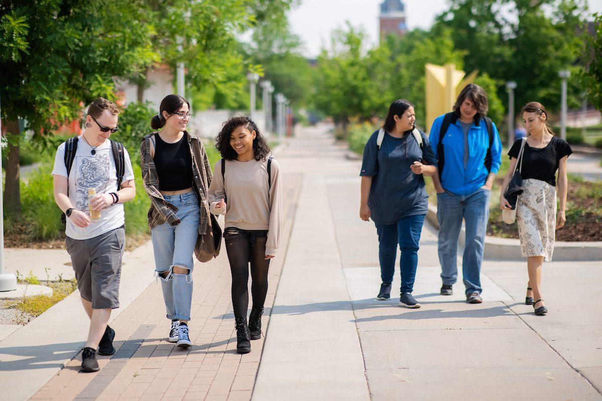 six students of walk together on a sidewalk near the library. en español: seis estudiantes de caminan juntos por una acera cerca de la biblioteca.