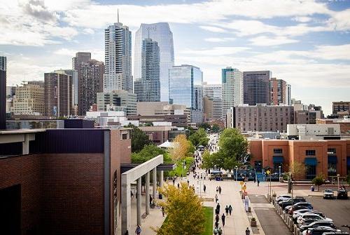 Aerial photo of students walking along Auraria Campus thoroughfare with Denver Downtown in background.